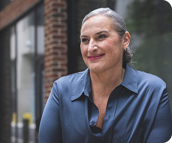 Lisa is a medium-light skin toned, feminine-presenting person with gray hair. She is outside and smiling.