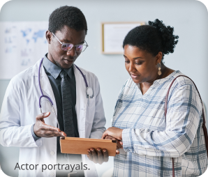 Two dark skin toned people, a patient and a doctor, looking at a tablet in a doctor's office. Actor portrayals.