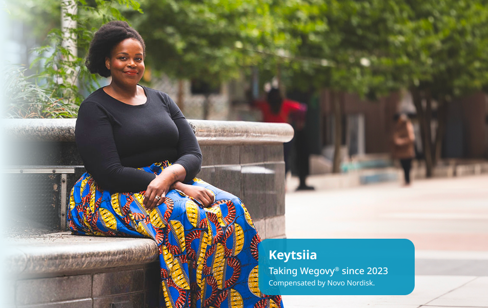 Keytsiia, dark-skinned and feminine-presenting, is seated outdoors, smiling. Keytsiia is a real person taking Wegovy since 2023.
