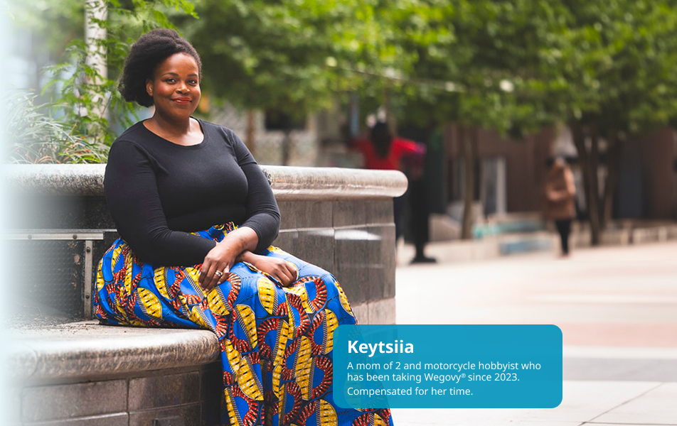 Keytsiia, dark-skinned and feminine-presenting, is seated outdoors, smiling. Keytsiia is a real person taking Wegovy since 2023.