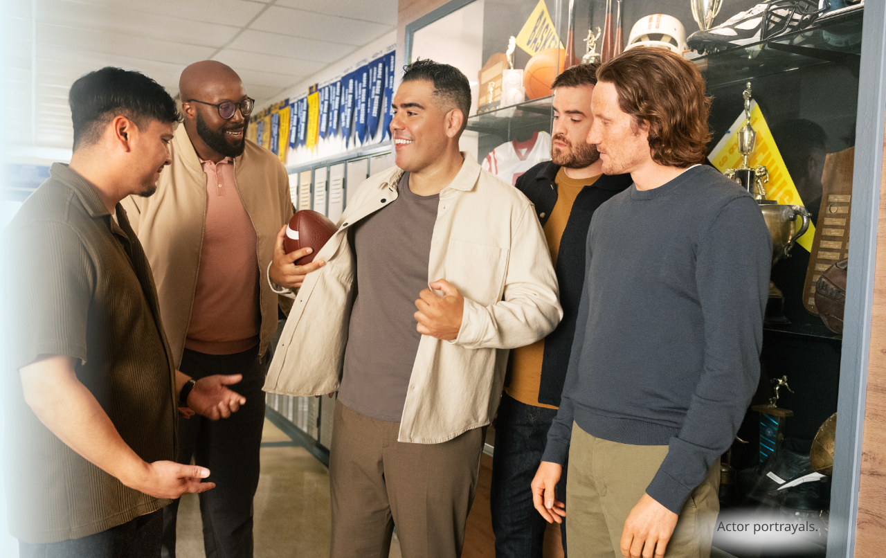 A dark skin toned, masculine-presenting person in their thirties standing in a record store and smiling. Actor portrayal.