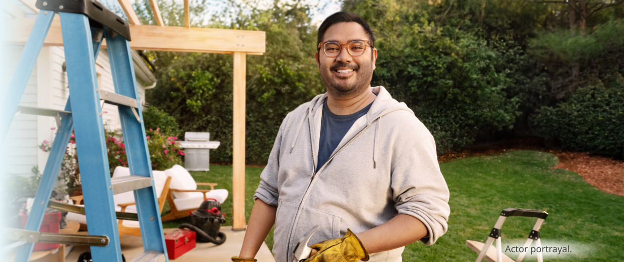 A medium skin toned, masculine-presenting person in their thirties working in their backyard and smiling. Actor portrayal.