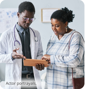 Two dark skin toned people, a patient and a doctor, looking at a tablet in a doctor's office. Actor portrayals.