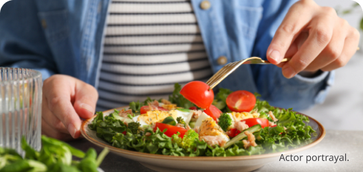 Light skin toned hands holding a fork over a bowl filled with colorful salad. Actor portrayal.​