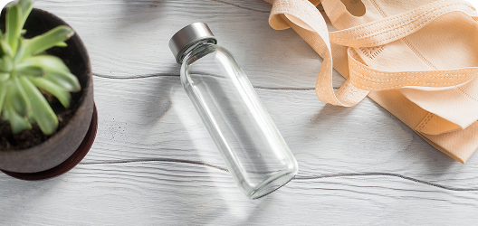 A water bottle lies next to a succulent and tote bag on a wooden kitchen counter.​