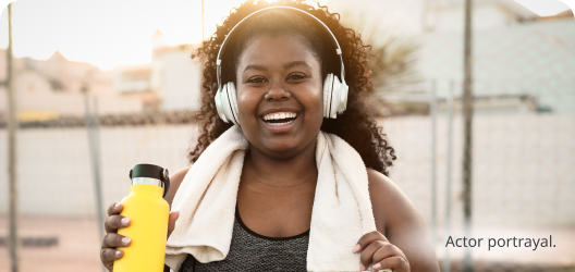 A young, dark skin toned, feminine-presenting person is smiling during a workout break. Actor portrayal.​